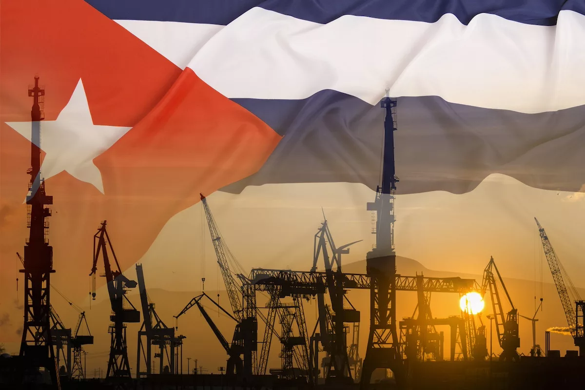 Oil wells silhouetted at sunset, set against a faded image of a Cuban flag