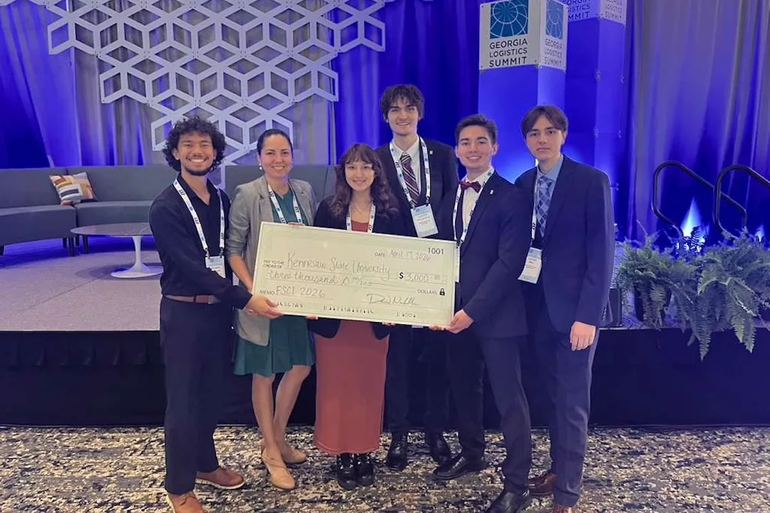 A group of students standing in front of a blue stage, and holding a large check