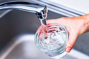 A hand holding a glass of water under a metal kitchen faucet