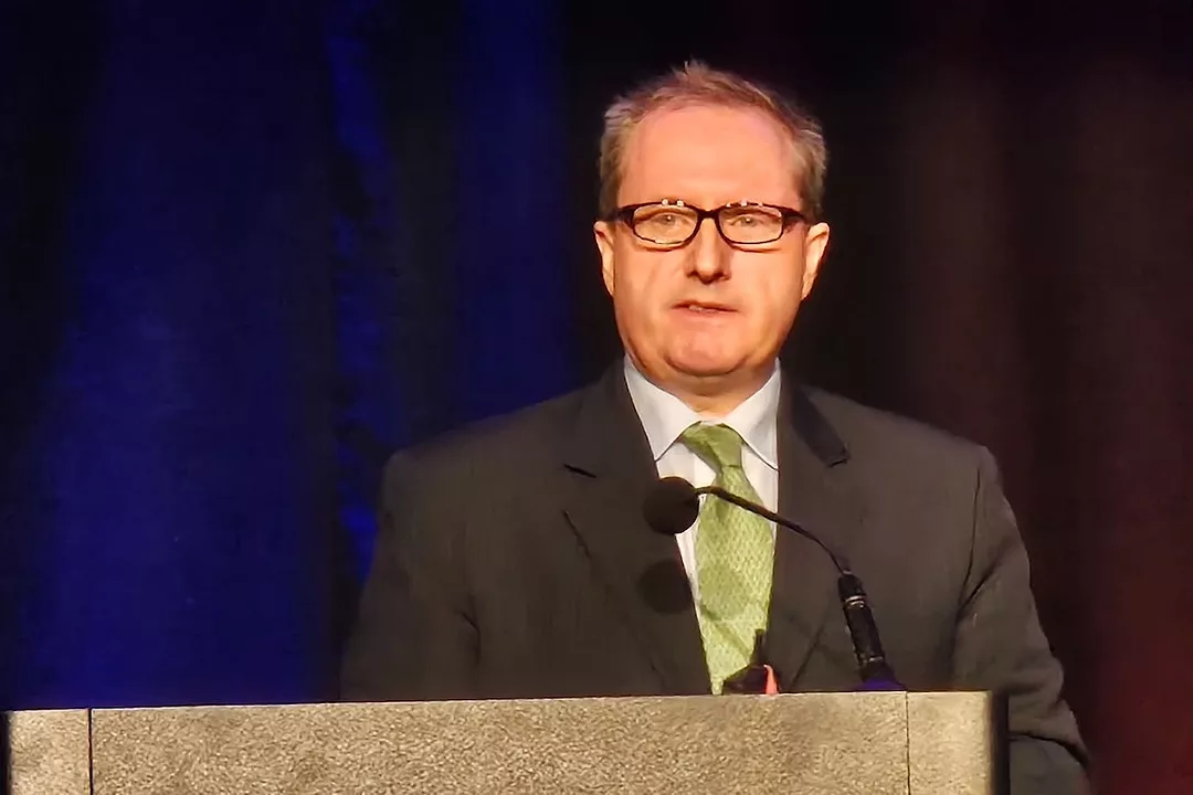 A man in a suit and a green tie standing at a podium