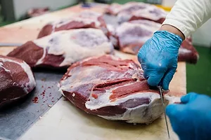 A WORKER TRIMS THE FAT FROM A MEAT CARCASS