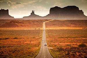 AN RV DRIVES DOWN A HIGHWAY TOWARD MONUMENT VALLEY UNDER A SETTING SUN