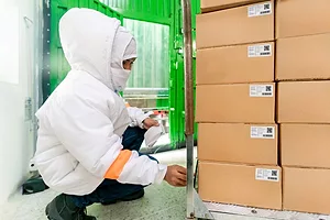 An employee in a warm suit crouches down to get boxes of food ready for shipping at a warehouse
