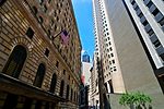 AN ARCHED STONE BUILDING FACES A CONCRETE AND GLASS SKYSCRAPER ACROSS A VERY NARROW STREET