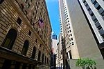 AN ARCHED STONE BUILDING FACES A CONCRETE AND GLASS SKYSCRAPER ACROSS A VERY NARROW STREET