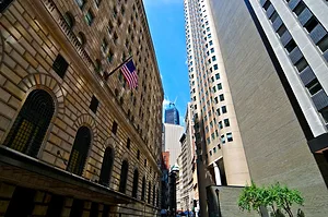 AN ARCHED STONE BUILDING FACES A CONCRETE AND GLASS SKYSCRAPER ACROSS A VERY NARROW STREET
