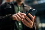 Close-up hands of unrecognizable man holding and using smartphone standing on city street.