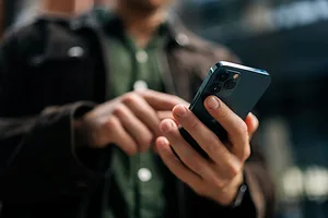 Close-up hands of unrecognizable man holding and using smartphone standing on city street.