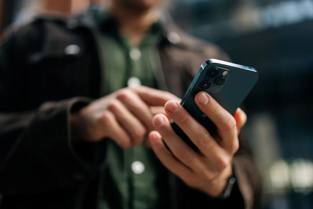 Close-up hands of unrecognizable man holding and using smartphone standing on city street.