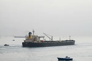 A SHIP PLIES A NARROW WATERWAY, FLANKED BY SMALLER BOATS