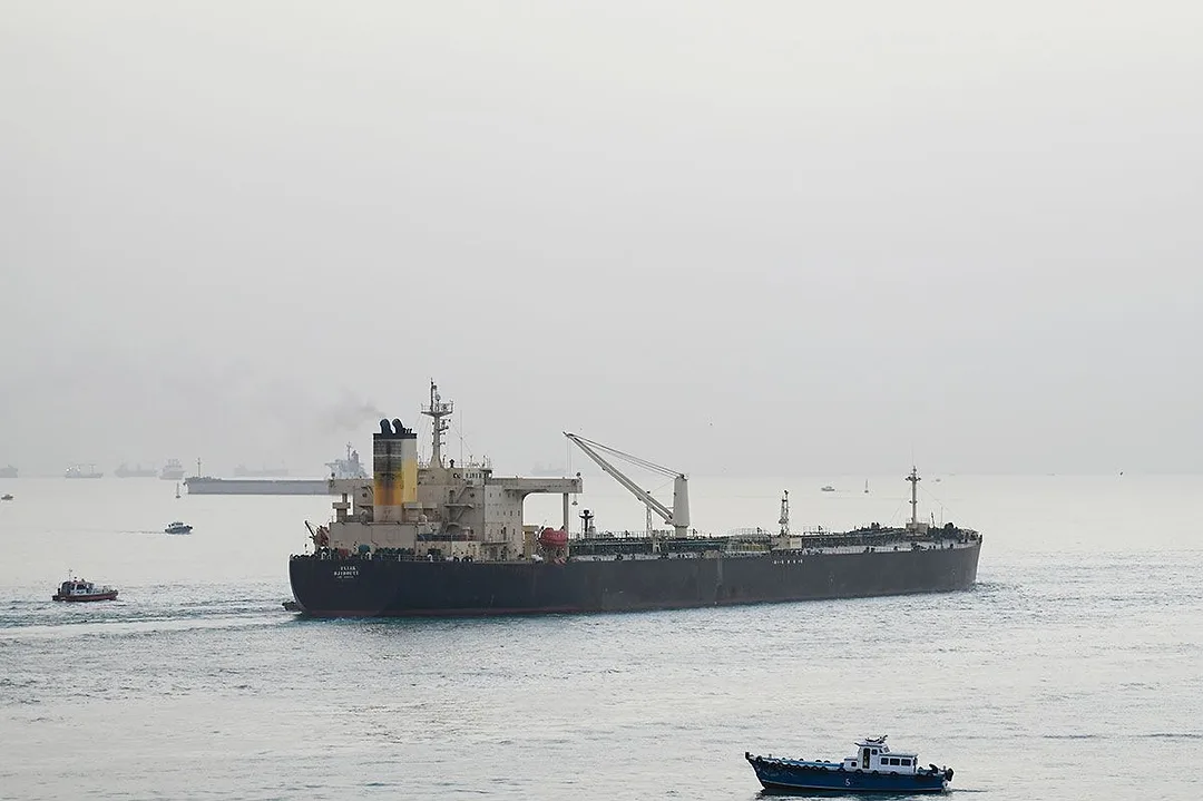 A SHIP PLIES A NARROW WATERWAY, FLANKED BY SMALLER BOATS