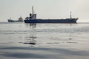 A SHIP SITS ON CALM SEA, ANOTHER SHIP VISIBLE BEHIND IT