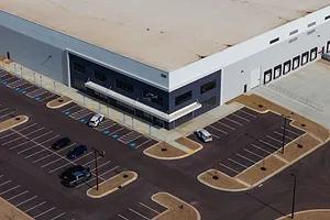 A FEW VEHICLES ARE PARKED IN A HUGE PARKING LOT OUTSIDE A WAREHOUSE