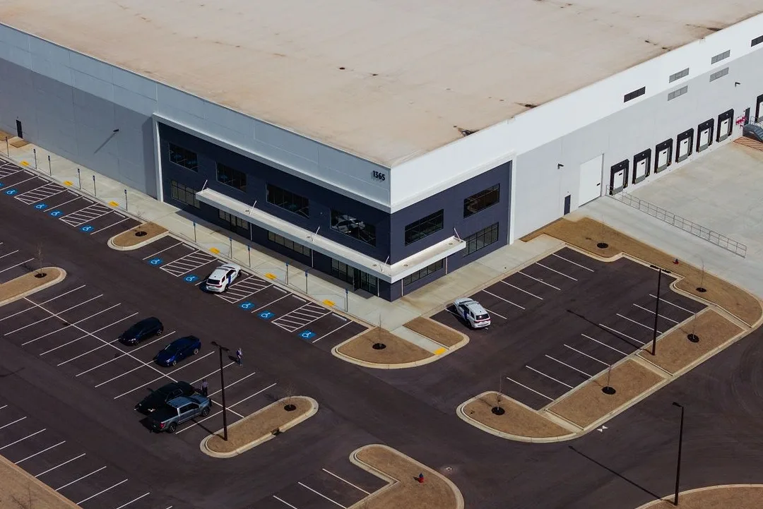 A FEW VEHICLES ARE PARKED IN A HUGE PARKING LOT OUTSIDE A WAREHOUSE
