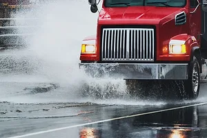 A red semi-truck driving through a puddle during a rainstorm