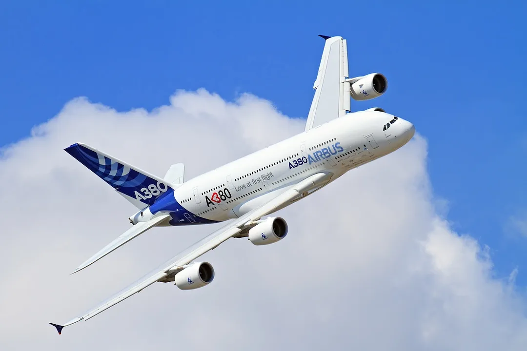 A white Airbus A380 passenger plane with a blue tail flies through the sky
