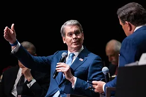 U.S. Treasury Secretary Scott Bessent in a navy blue suit, speaking into a microphone with one arm raised