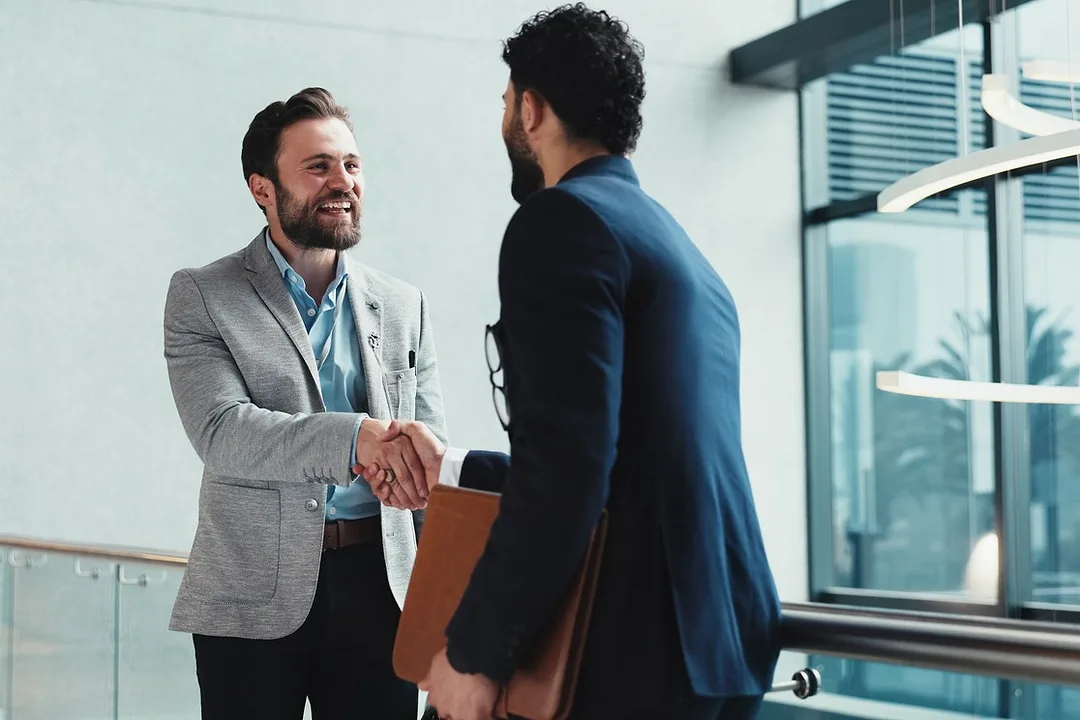 TWO BEARDED MEN IN SUITS SHAKE HANDS ENTHUSIASTICALLY