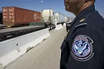 A UNIFORMED OFFICER STANDS NEAR A HIGHWAY WITH TRUCKS ON IT