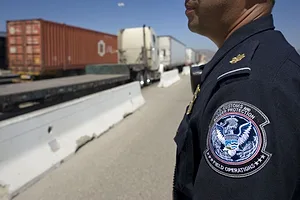A UNIFORMED OFFICER STANDS NEAR A HIGHWAY WITH TRUCKS ON IT