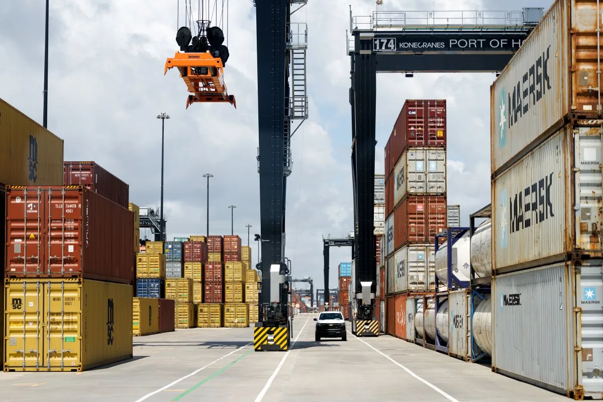 A CRANE HOVERS ABOVE A STACK OF CONTAINERS ON A BUSY PORT DOCK