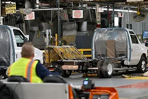 A WORKER IN A HI-VIS VEST DRIVES A VEHICLE INTO AN INDUSTRIAL WORKSPACE