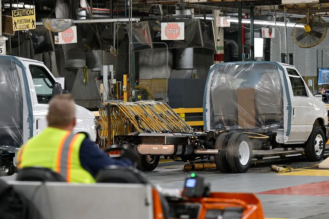 A WORKER IN A HI-VIS VEST DRIVES A VEHICLE INTO AN INDUSTRIAL WORKSPACE
