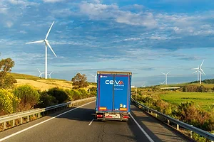 A Truck with the logo of the CEVA Logistics company drives down a highway flanked with windpower towers.