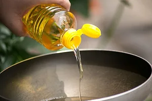 A hand pours food oil in a hot pan for deep frying