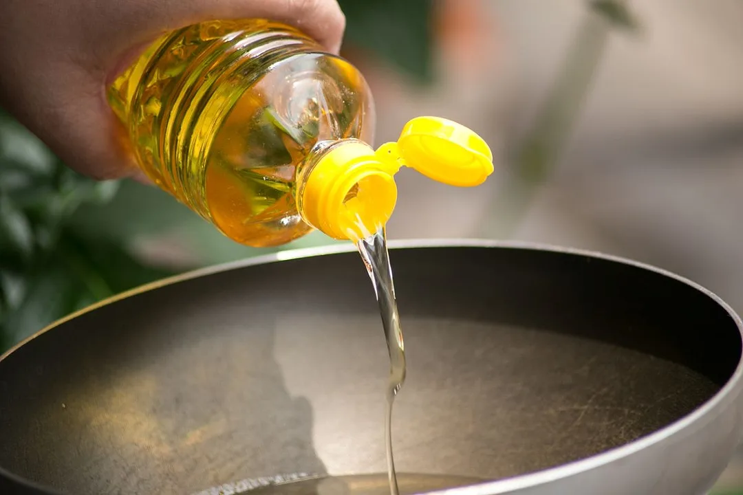 A hand pours food oil in a hot pan for deep frying