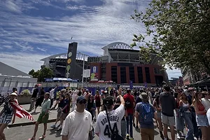 A crowd of fans outside of a red brick football stadium on a sunny day