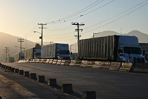 A LINE OF TRUCKS SIT ON A HIGHWAY IN MORNING LIGHT, MOUNTAINS VISIBLE IN THE BACKGROUND