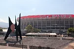 A grey concrete soccer stadium with a red lining around the upper edge of the bowl