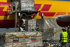 LARGE SHIPMENTS SHRINK-WRAPPED IN BROWN PLASTIC ARE LOADED FROM A PLANE BEARING THE DHL LOGO IN YELLOW AND RED