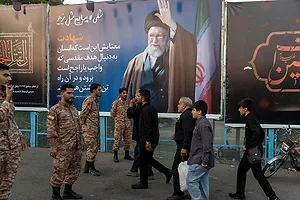 PEDESTRIANS AND SOLDIERS PASS BY A LARGE POSTER FEATURING A SHIITE MUSLIM CLERIC