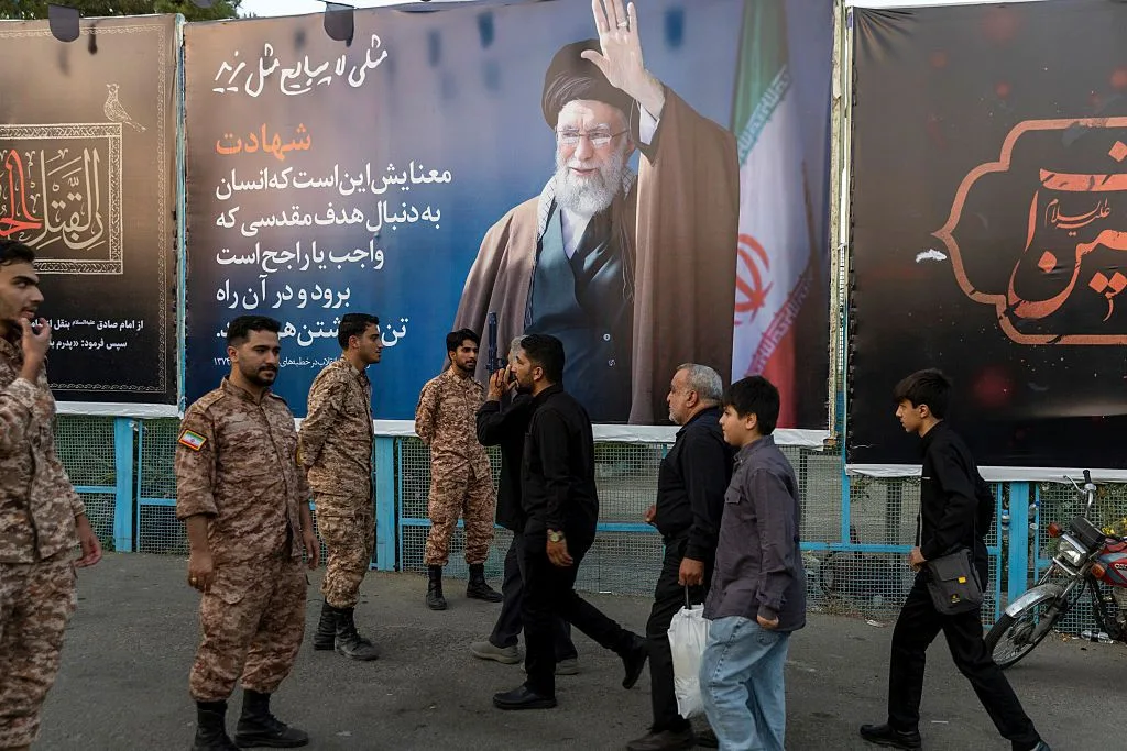 PEDESTRIANS AND SOLDIERS PASS BY A LARGE POSTER FEATURING A SHIITE MUSLIM CLERIC