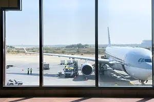 A LARGE PLANE IS VISIBLE ON THE TARMAC THROUGH THE WINDOWS OF AN AIRPORT TERMINAL