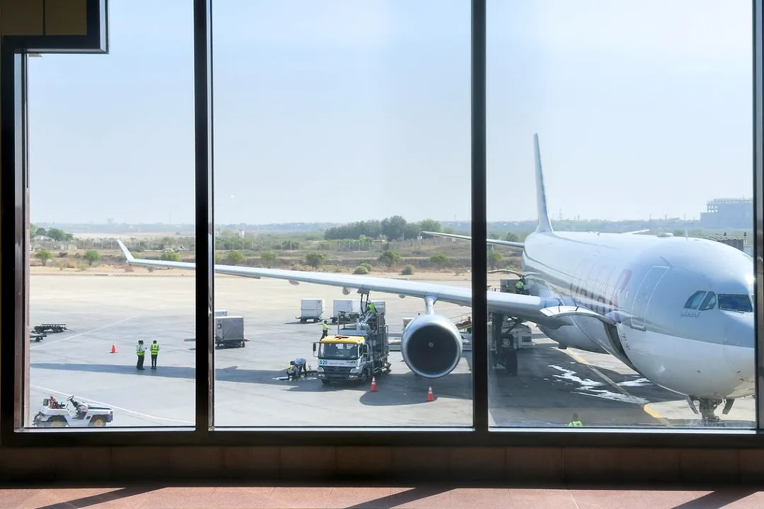 A LARGE PLANE IS VISIBLE ON THE TARMAC THROUGH THE WINDOWS OF AN AIRPORT TERMINAL