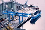 A blue container ship docked at a port beneath a blue shipping crane