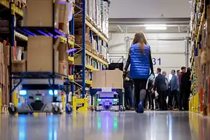 A PICKER WORKS WITH ROBOTS IN THE STACKS OF A WAREHOUSE