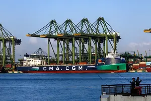 A SHIP BEARING THE LETTERS CMA CGM DOCKS AT A PORT UNDER MULTIPLE CRANES