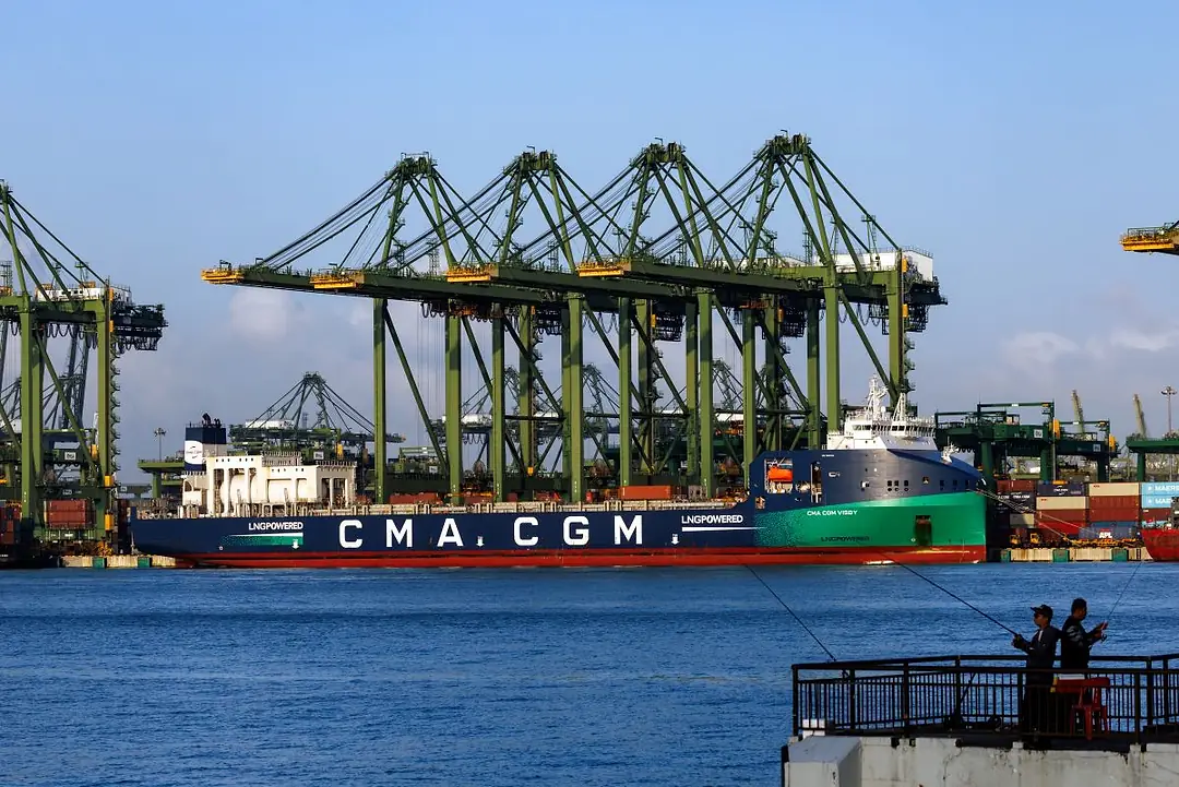 A SHIP BEARING THE LETTERS CMA CGM DOCKS AT A PORT UNDER MULTIPLE CRANES