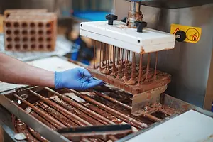 A mold on an assembly line dripping chocolate onto a tray below