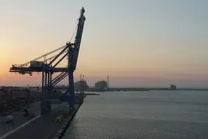 A large gantry crane along a shoreline at sunset