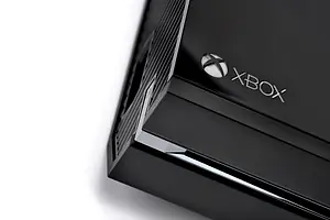 The corner of a rectangular black gaming console, with an "XBOX" logo printed along the edge