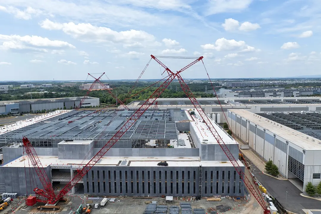 A white warehouse building under construction, with red cranes towering over the top