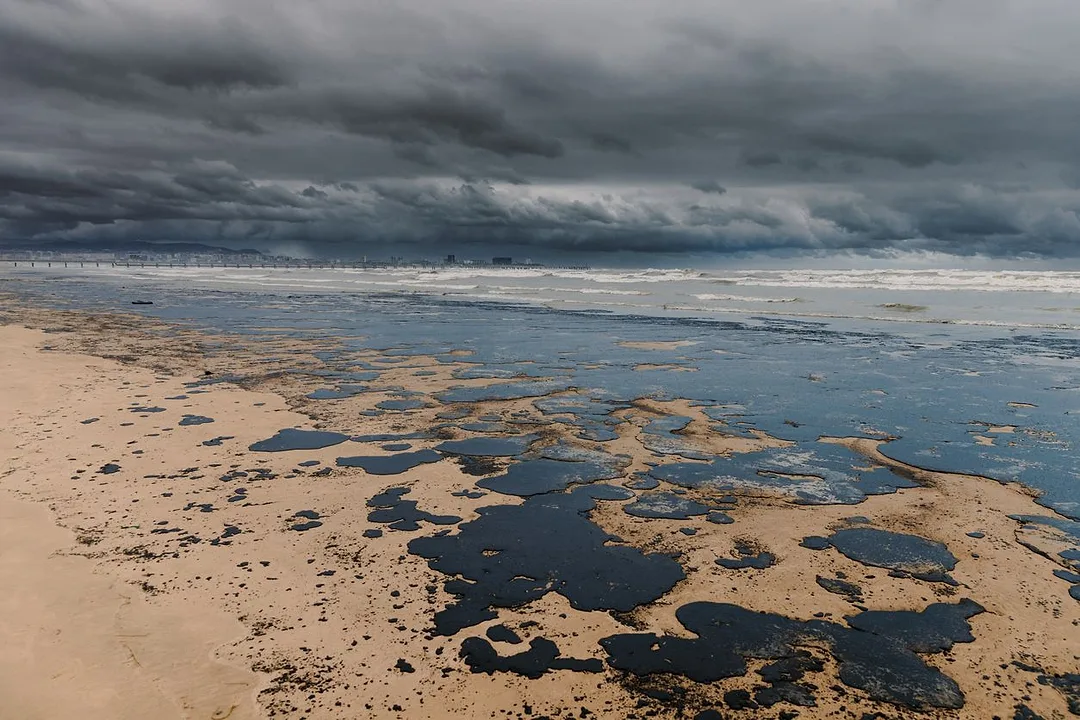 BLACK PUDDLES OF OIL FORM ON AN EMPTY BEACH UNDER STORMY SKIES