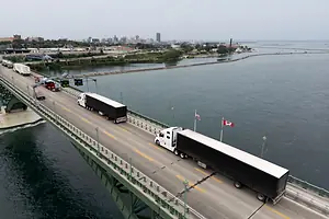 TRUCKS CROSS A BRIDGE OVER WATER, A CITY SKYLINE IN THE DISTANCE