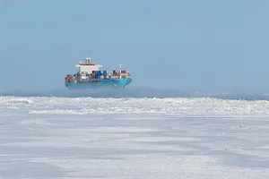 A blue container ship pushes through icy waters