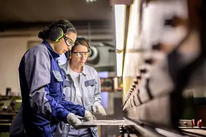 Mature and a Young Female Coworkers Inspecting Press Brake Machine